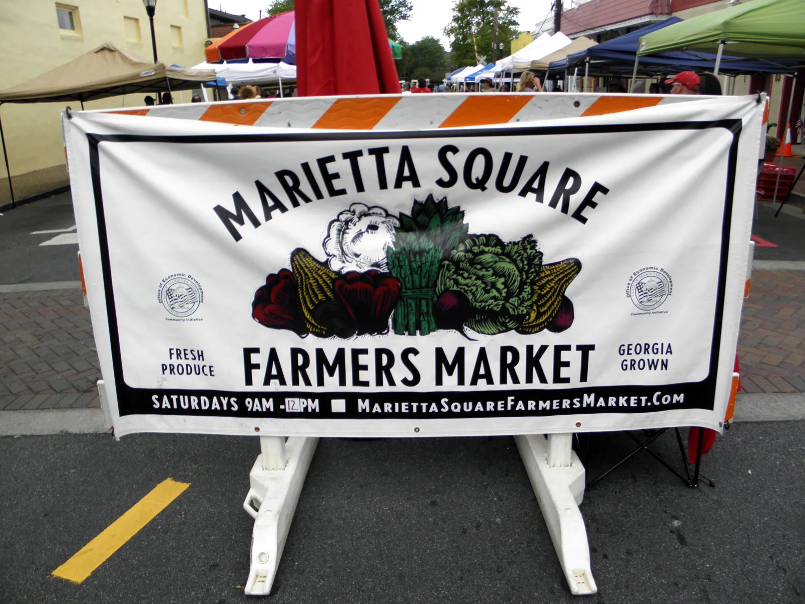 The Marietta Square Farmers Market banner in front of a row of vendor tents in downtown Marietta.
