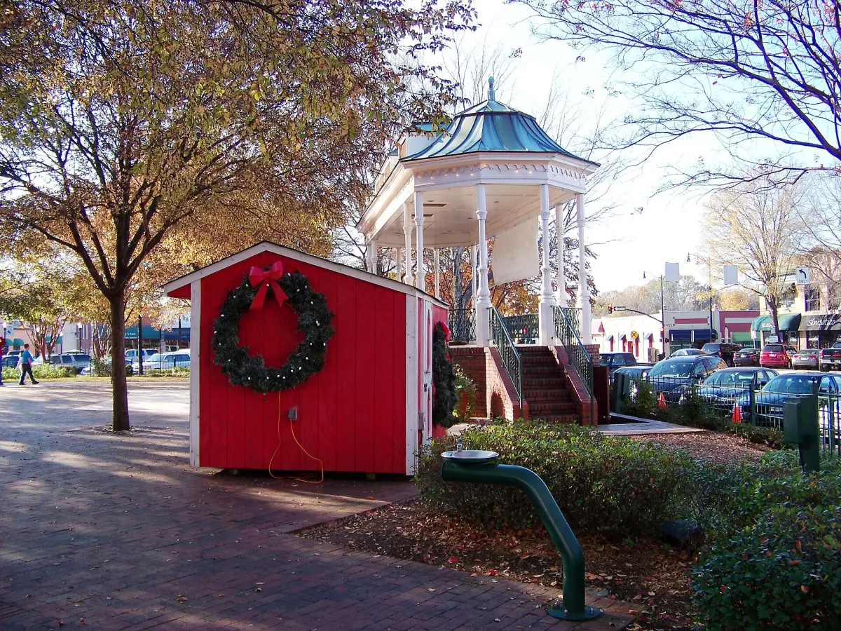 A red holiday hut hung with a wreath beside the gazebo in Glover Park on Marietta Square