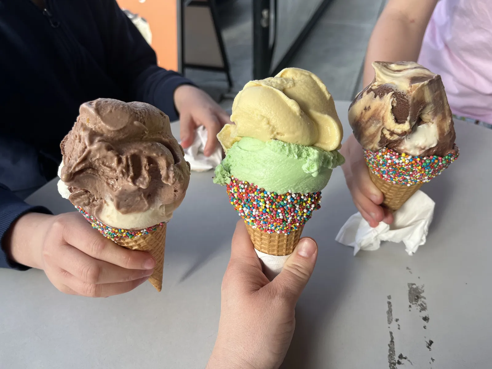 Three ice cream cones, two with sprinkles, held over a table. The photo was not taken in Marietta.